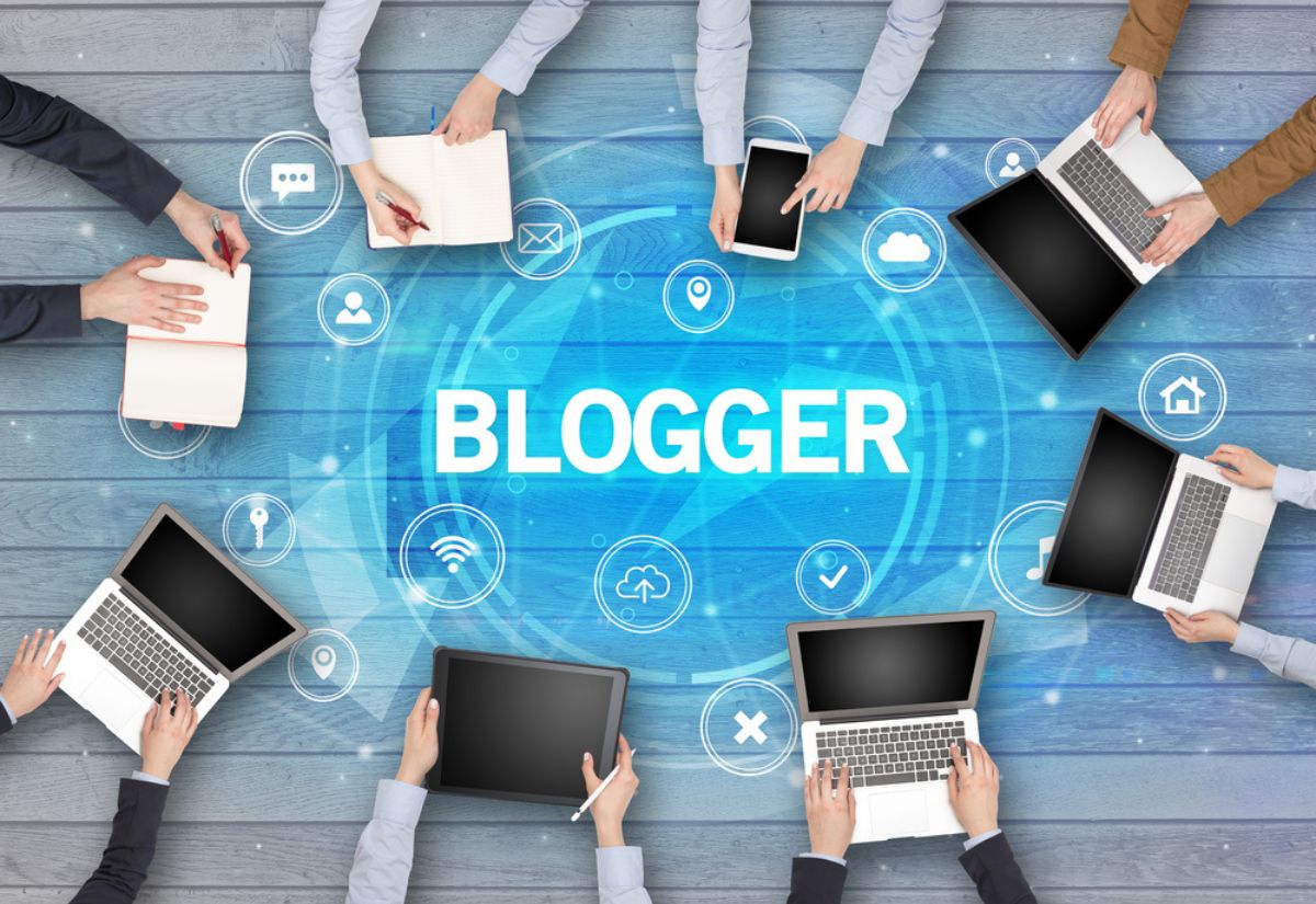 Multiple hands with laptops and notebooks around the word "BLOGGER," surrounded by network icons representing digital communication.