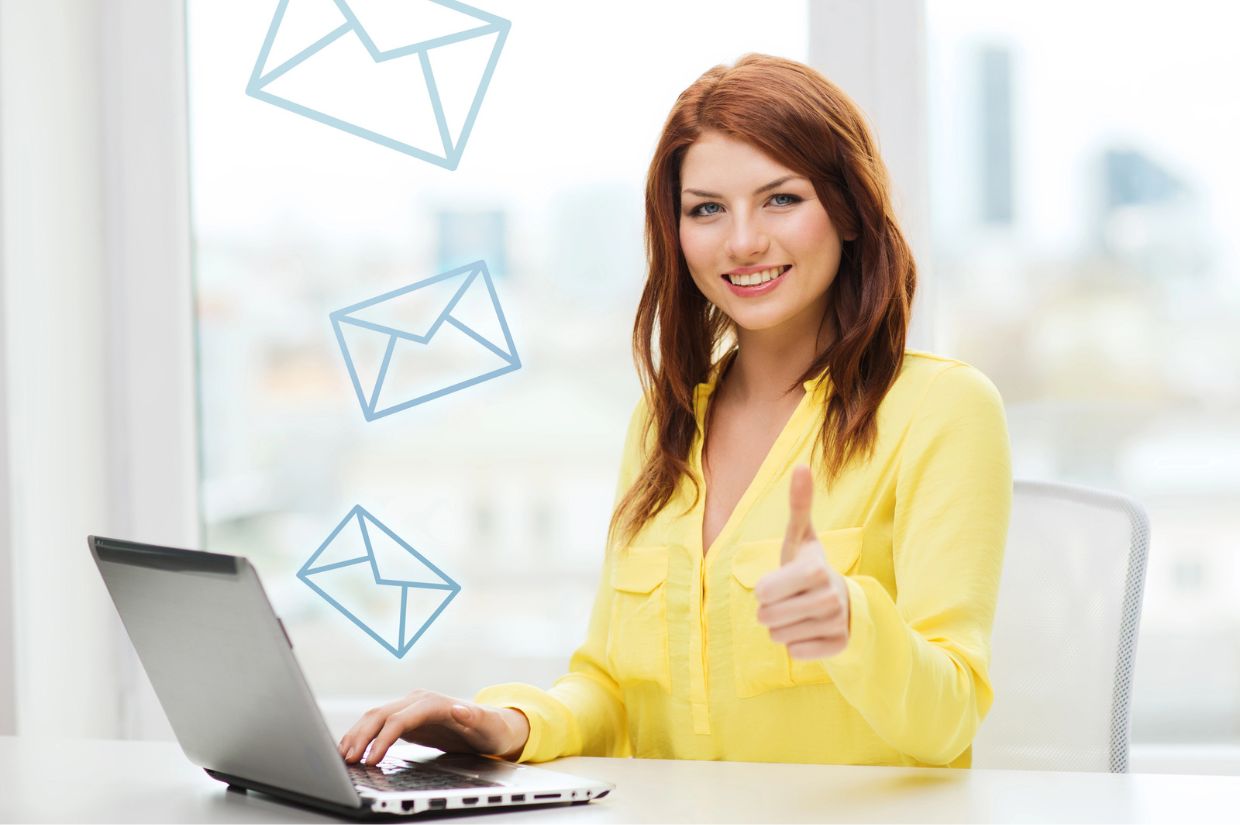A person in a yellow shirt sits at a laptop, giving a thumbs up with email icons floating above, symbolizing positivity and communication.