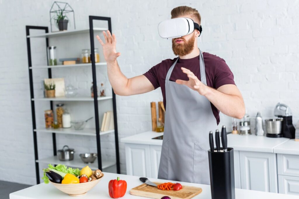 Young man in apron using virtual reality headset while cooking in kitchen.