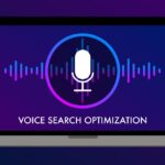 Illustration of a laptop screen displaying a microphone icon within a circular outline, surrounded by soundwave graphics in gradient shades of purple, blue, and pink. Below the icon, the text reads 'Voice Search Optimization' on a dark purple background.