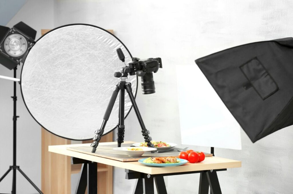 A professional food photography setup in a studio, featuring a camera on a tripod aimed at plated dishes on a wooden table.