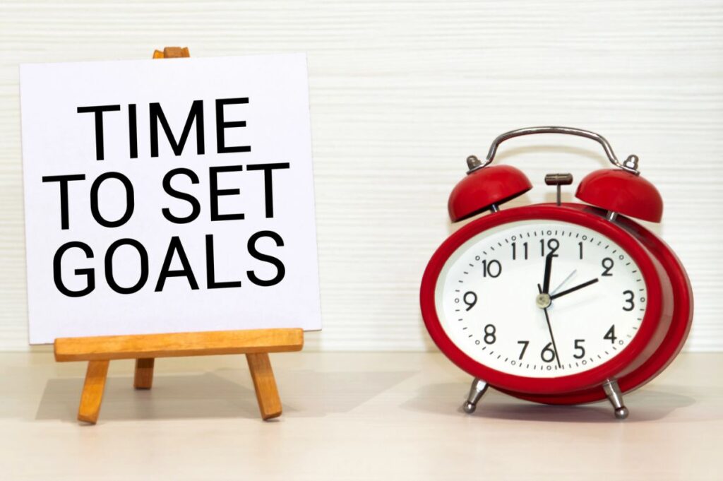 A white sign on a small wooden easel displays the words "TIME TO SET GOALS" in bold black letters.